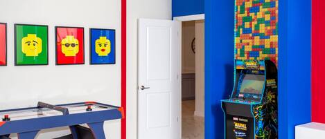 A room with a foosball table, a wall-mounted video game console, and framed artwork on the wall.