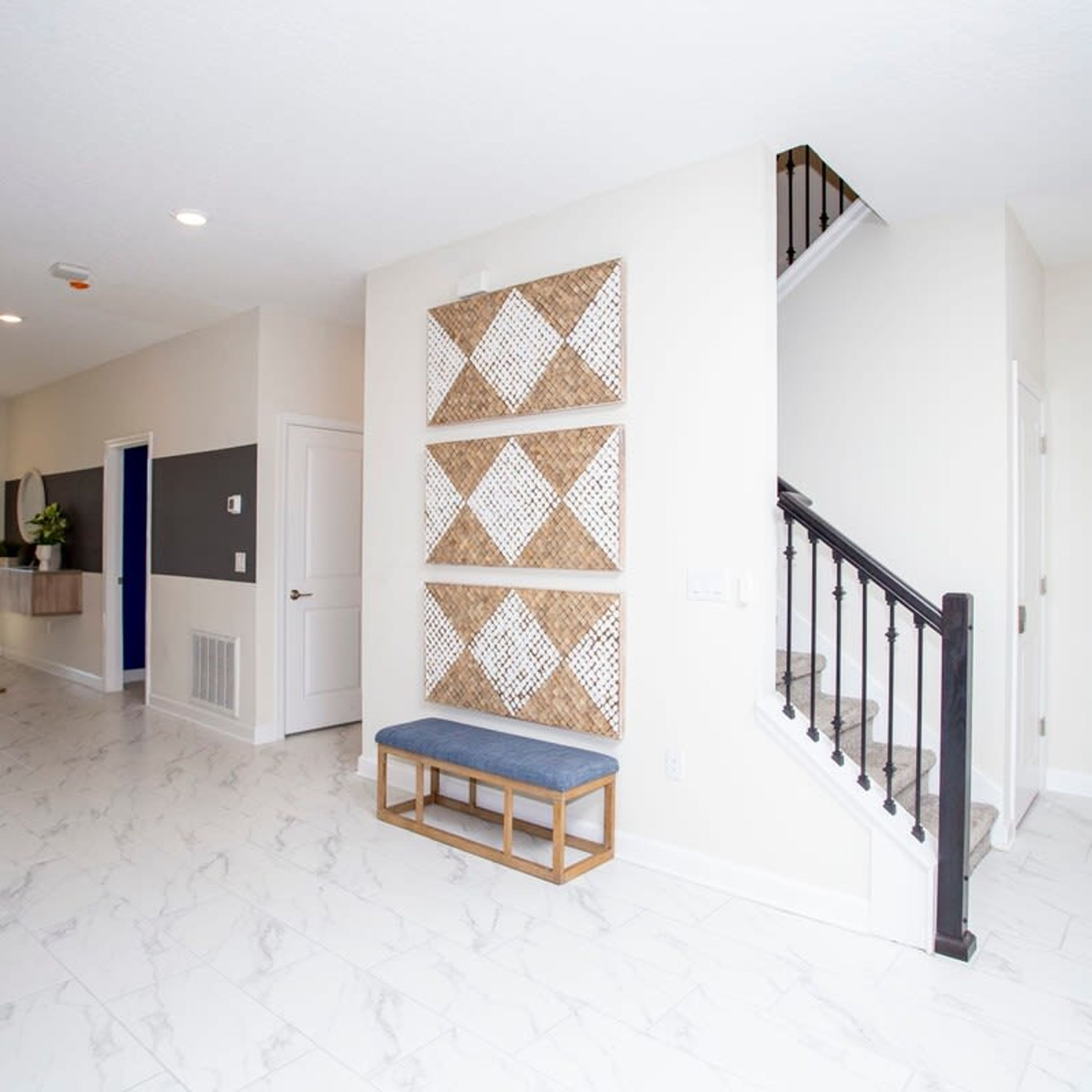 A spacious hallway with a marble floor, a wooden bench, and a staircase with a black railing.