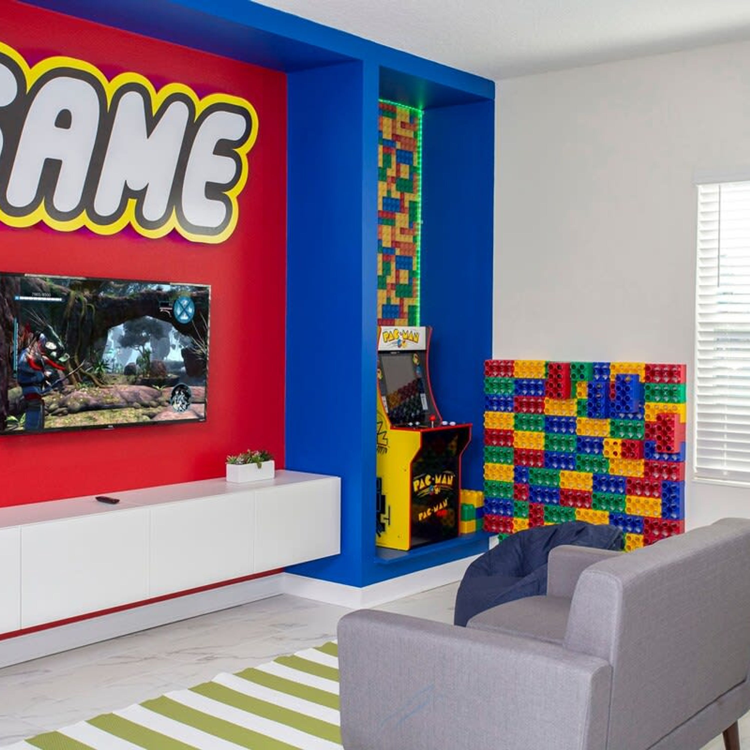 A modern living room with a large TV, a Pac-Man arcade machine, and a colorful LEGO wall.