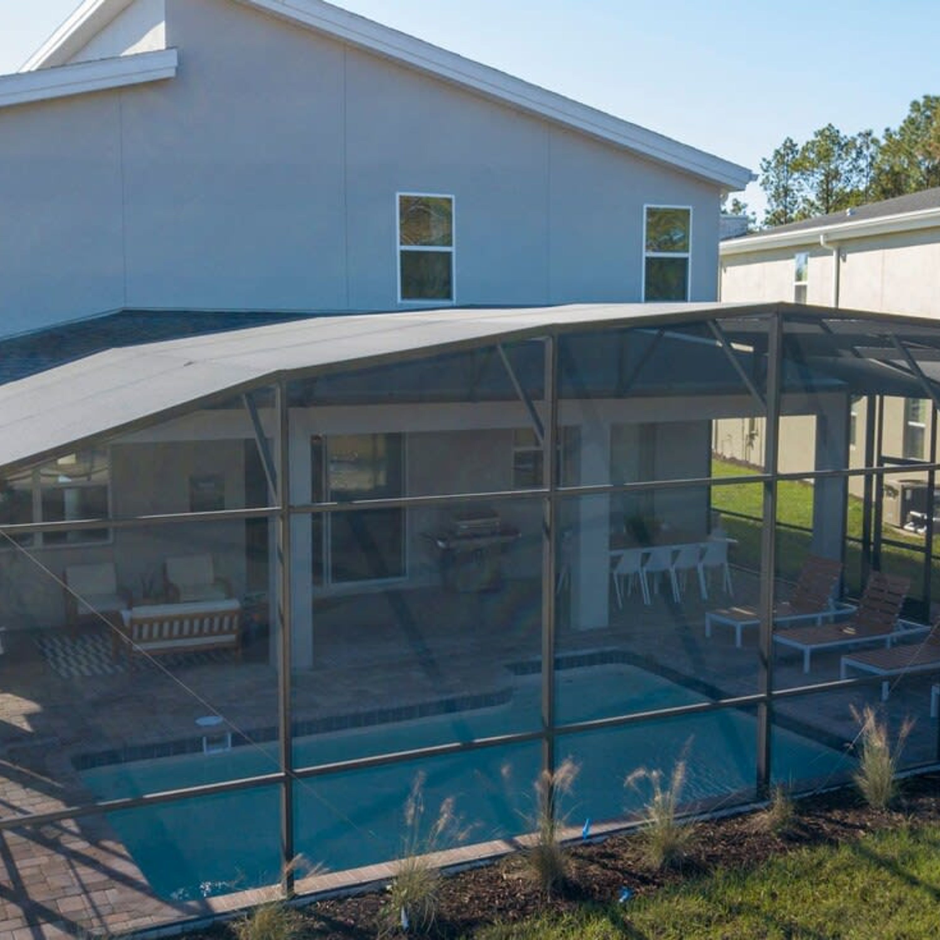 Una casa moderna con zona de piscina exterior cubierta, paredes de vidrio y un patio con sillones de descanso.