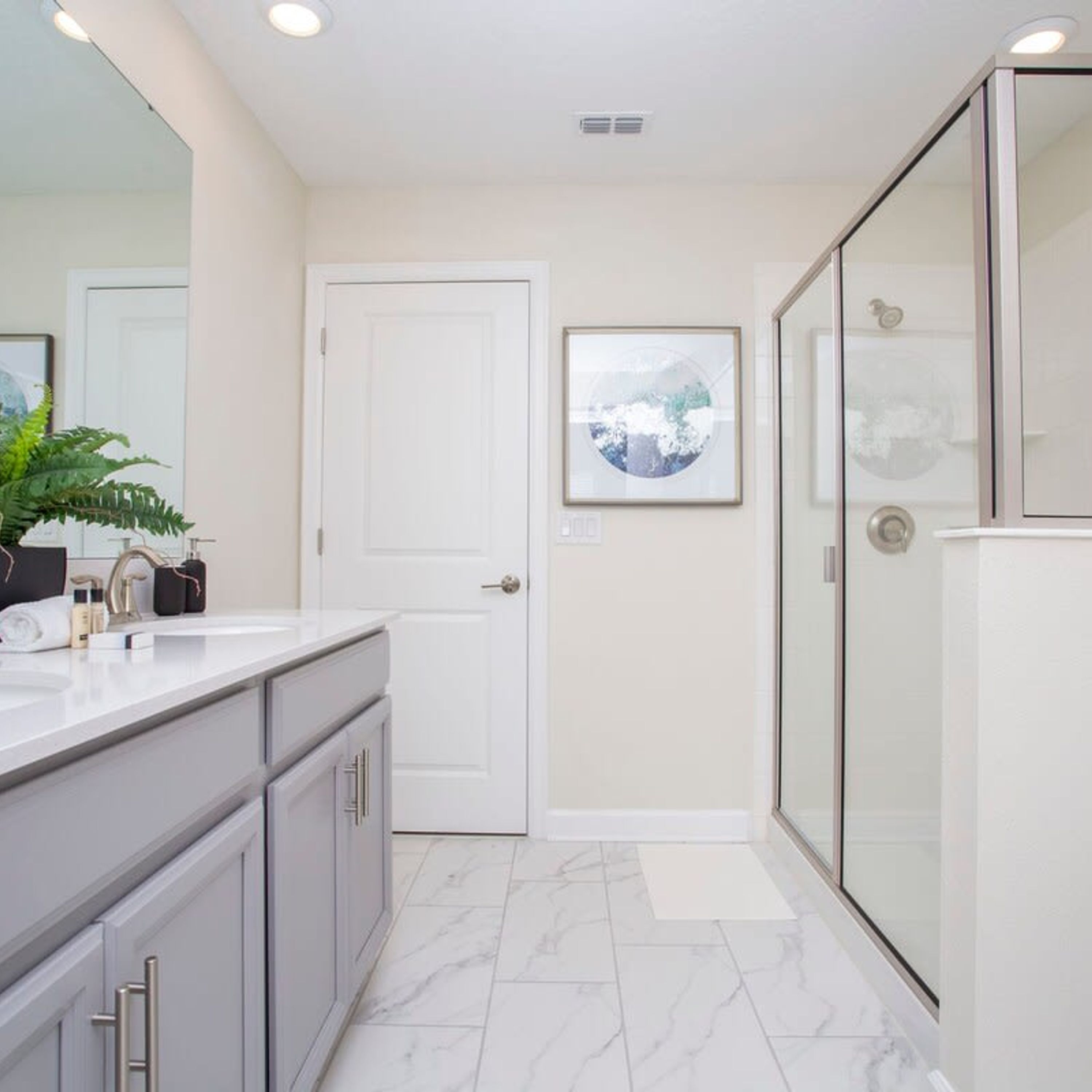 A modern bathroom with a white vanity, a glass shower enclosure, and a door with a framed picture.