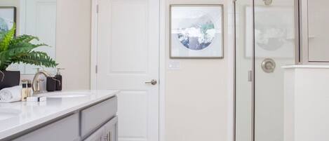 A modern bathroom with a white vanity, a glass shower enclosure, and a door with a framed picture.