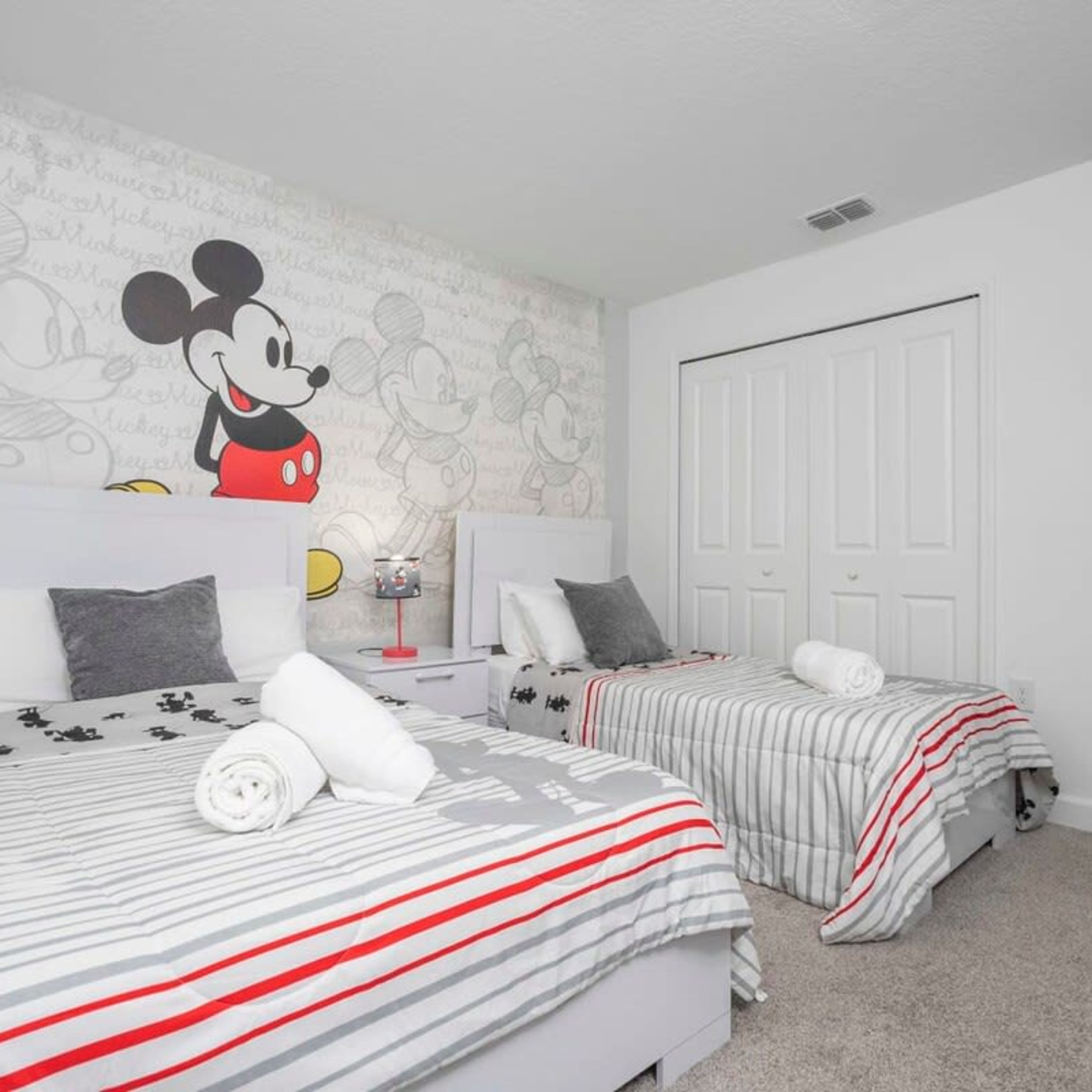 Une chambre d’hôtel avec deux lits, chacun agrémenté de draps à rayures et d’une décoration sur le thème de Mickey Mouse.