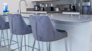 Una cocina moderna con armarios blancos, electrodomésticos de acero inoxidable y una isla central con taburetes de bar.
