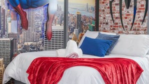 Un dormitorio con un gran mural de Spider-Man, una pared de ladrillo y vistas a la ciudad.