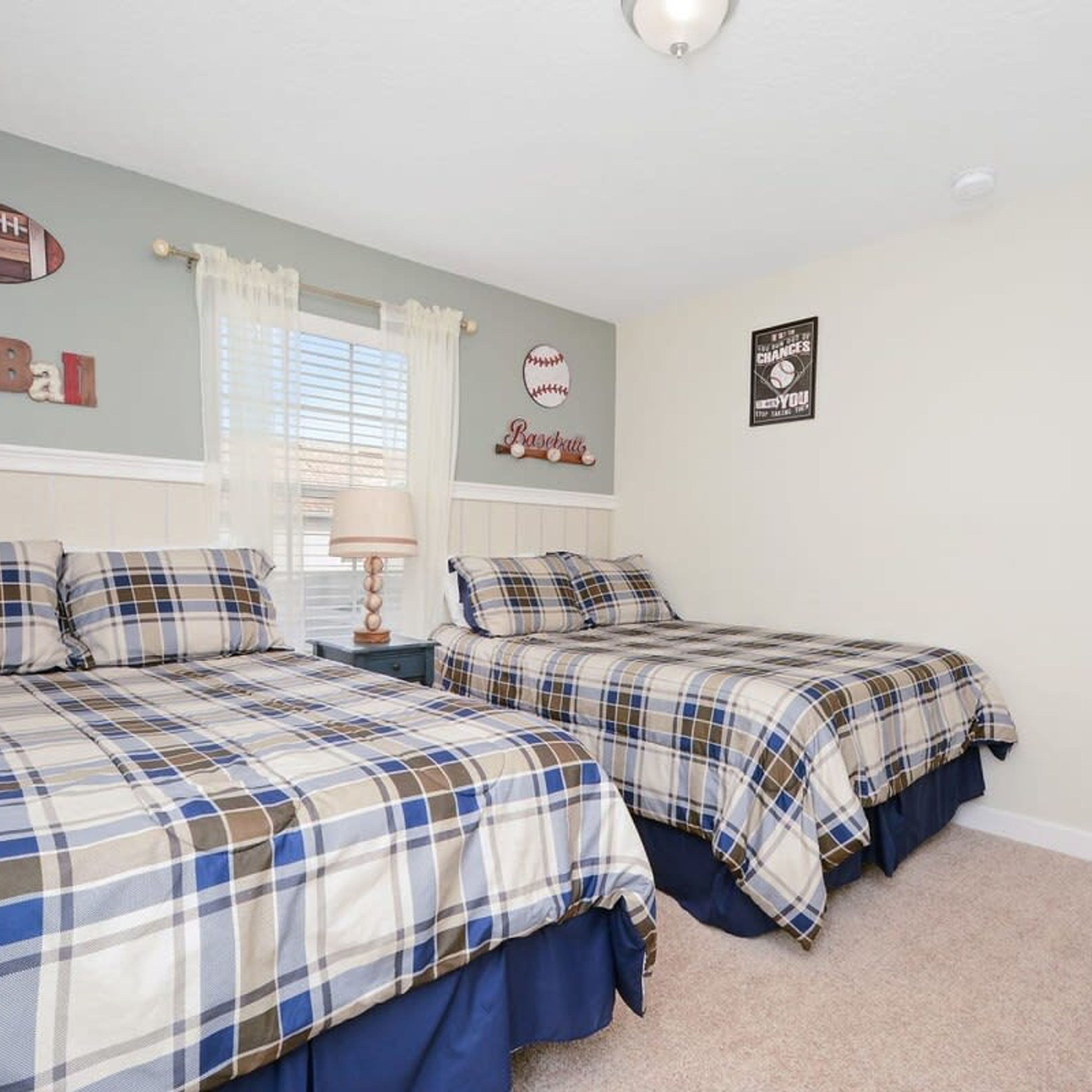 A bedroom with two beds, a window with curtains, and wall decorations including a baseball theme and a motivational quote.
