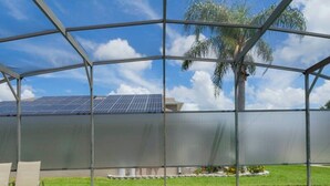A swimming pool with a glass enclosure, a palm tree, and solar panels in the background. - 150 Stunning 4BD Perfect for Your Vacation (Davenport)