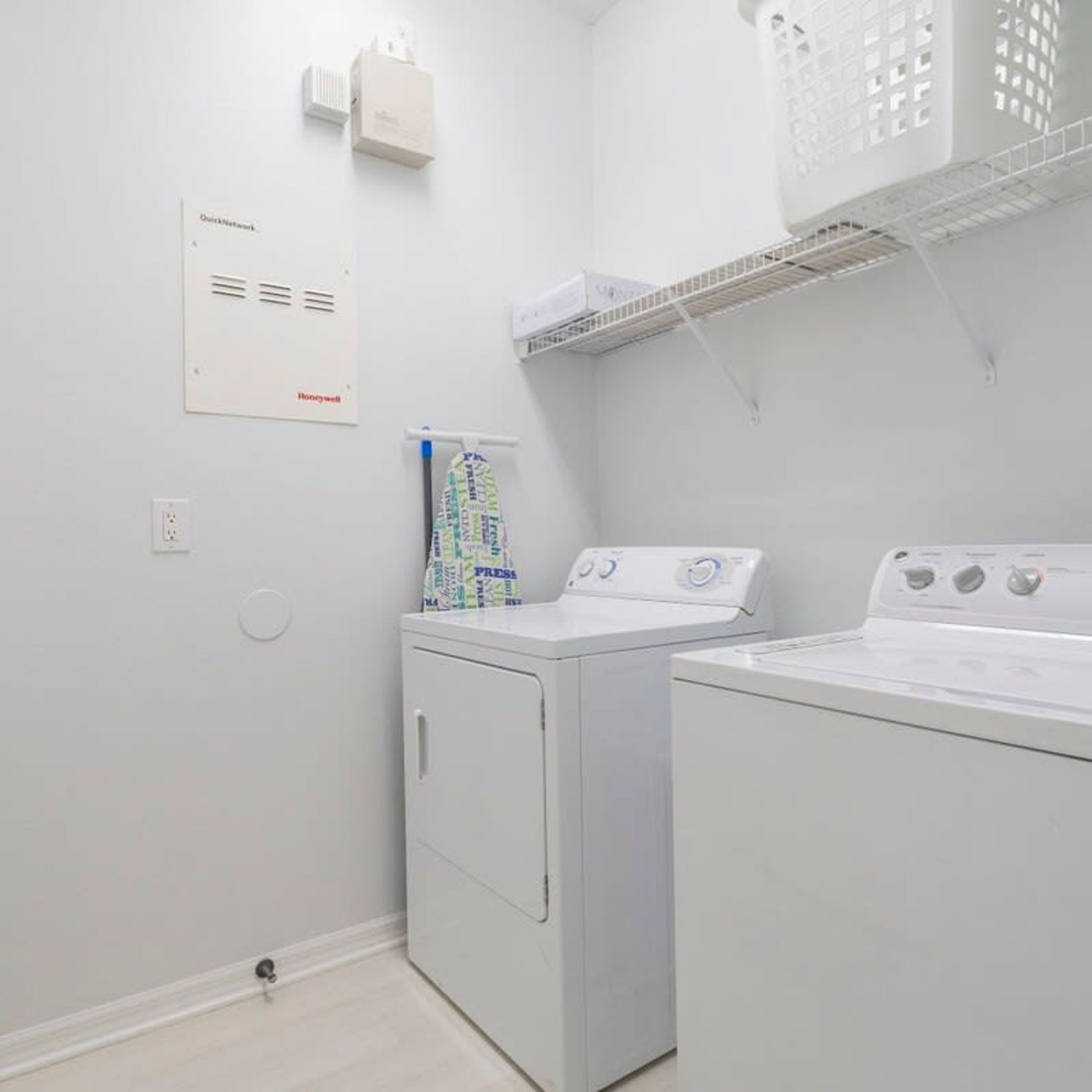 A laundry room with a front-loading washer and dryer, a wall-mounted heater, and a shelf above the dryer.