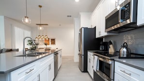A modern kitchen with white cabinetry, stainless steel appliances, and pendant lighting. - 2681 Stunning 4BD Home Perfect For Your Family (Kissimmee)