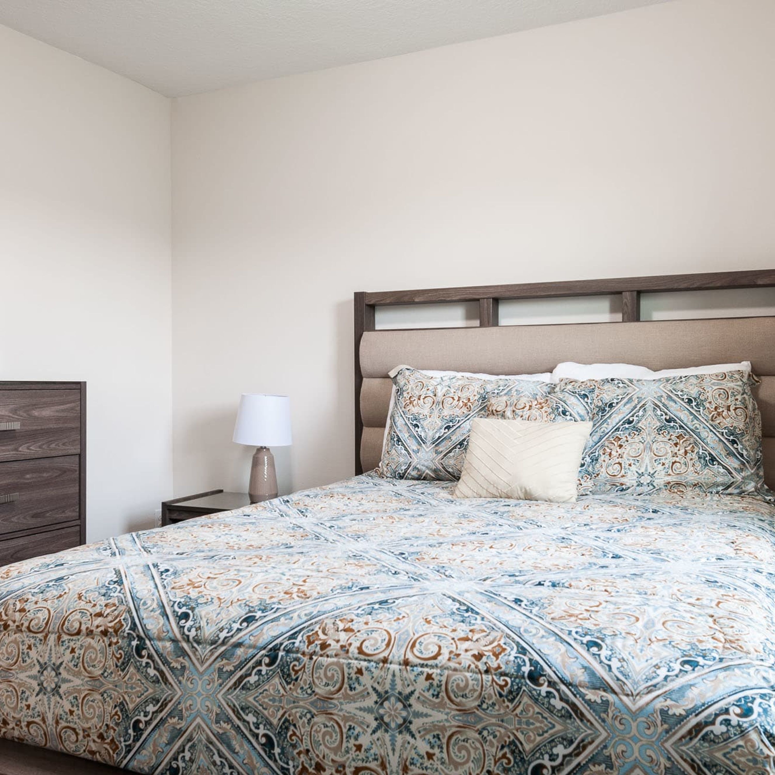 Une chambre à coucher avec un lit, une table de chevet, une lampe et une commode en bois.