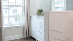 A bathroom with a large window, white cabinets, a mirror, and a shower area. - 4449 Lovely 5BD For Your Family (Kissimmee)