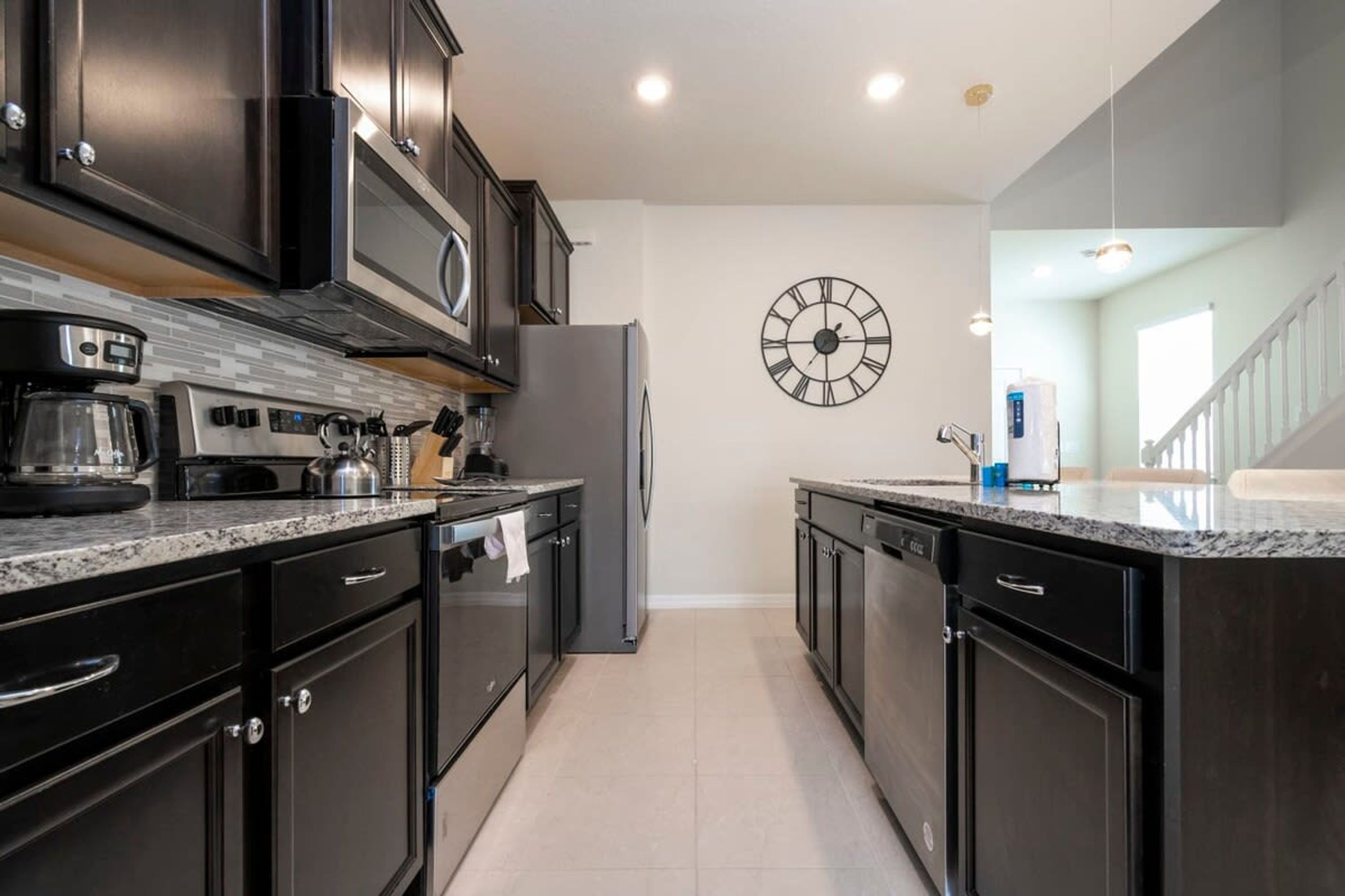 A modern kitchen with dark cabinetry, a stainless steel refrigerator, a coffee maker, and a clock on the wall.