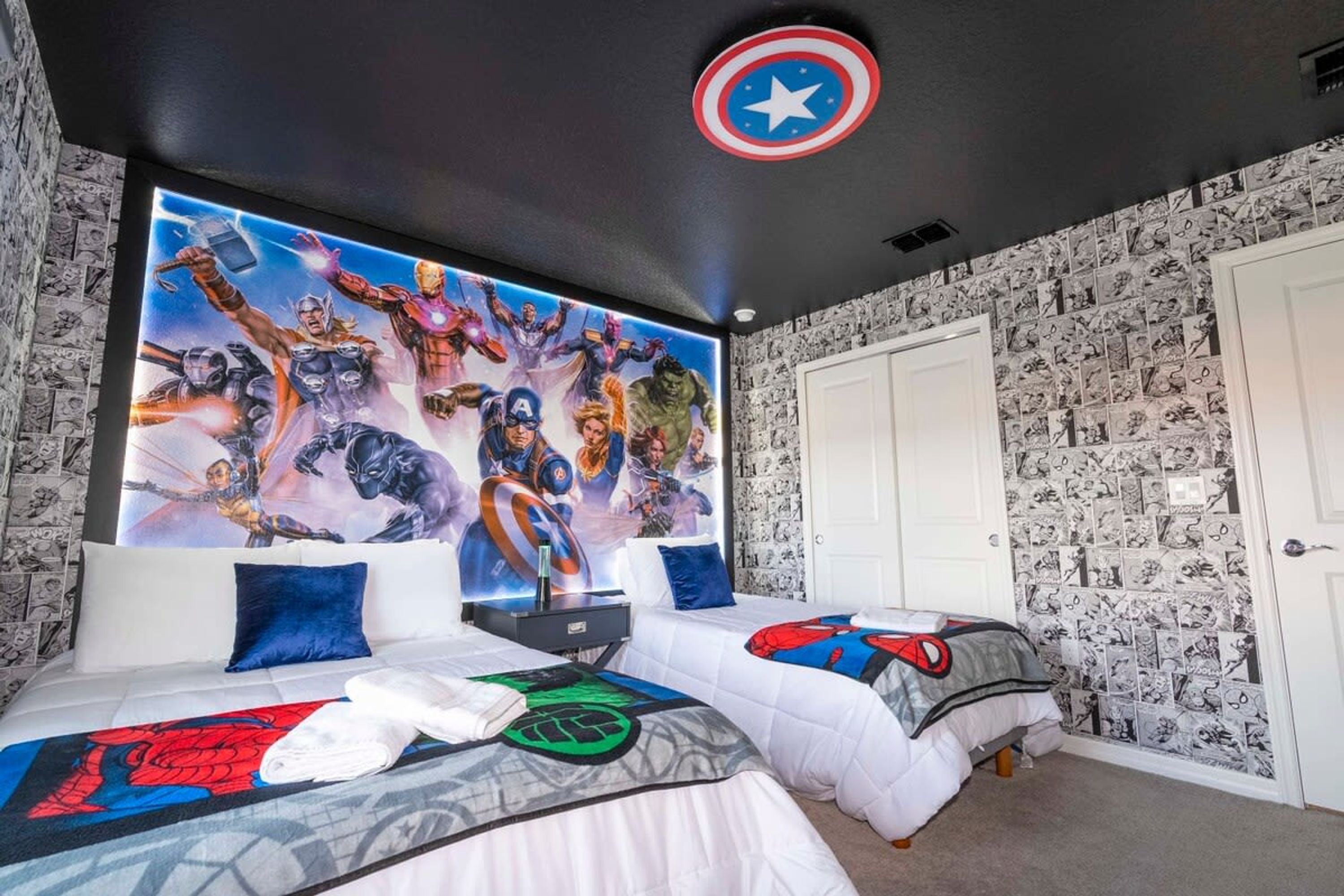 A bedroom with two beds, a large superhero-themed mural, and a Captain America shield on the ceiling.