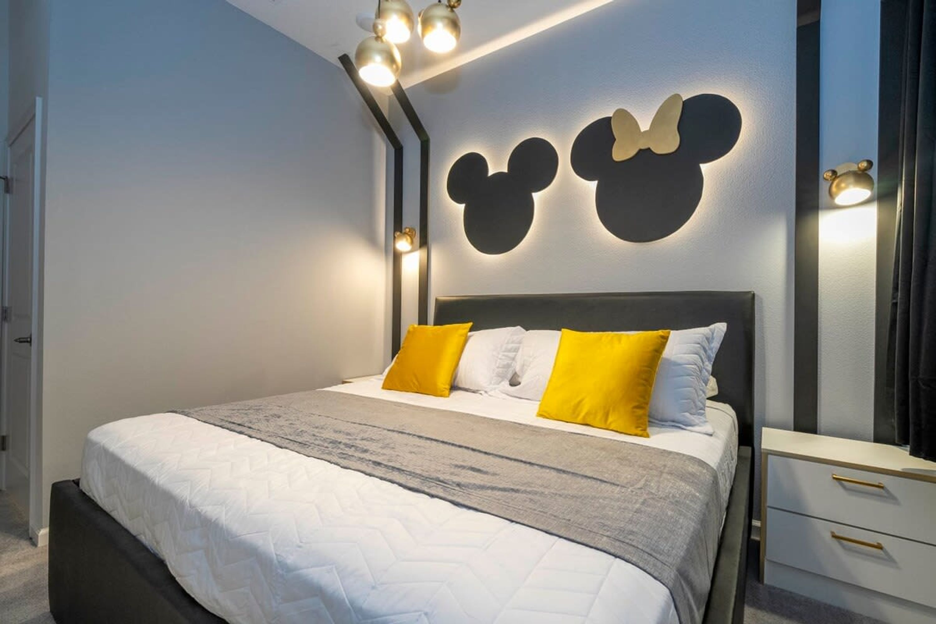 A modern bedroom with a bed, a nightstand, and a Mickey Mouse wall decoration.