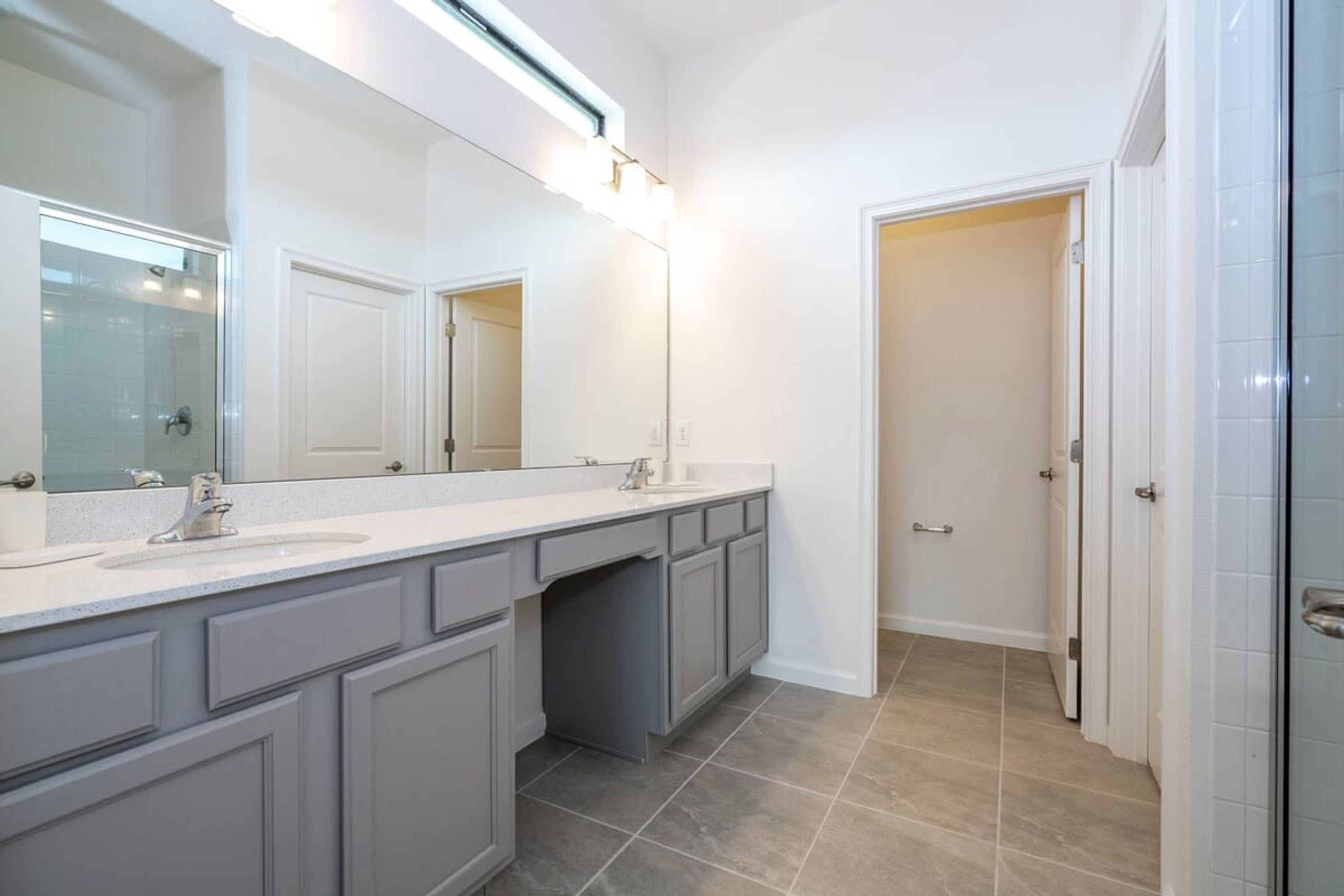 Un baño moderno con un tocador amplio, lavamanos doble y ducha a pie.