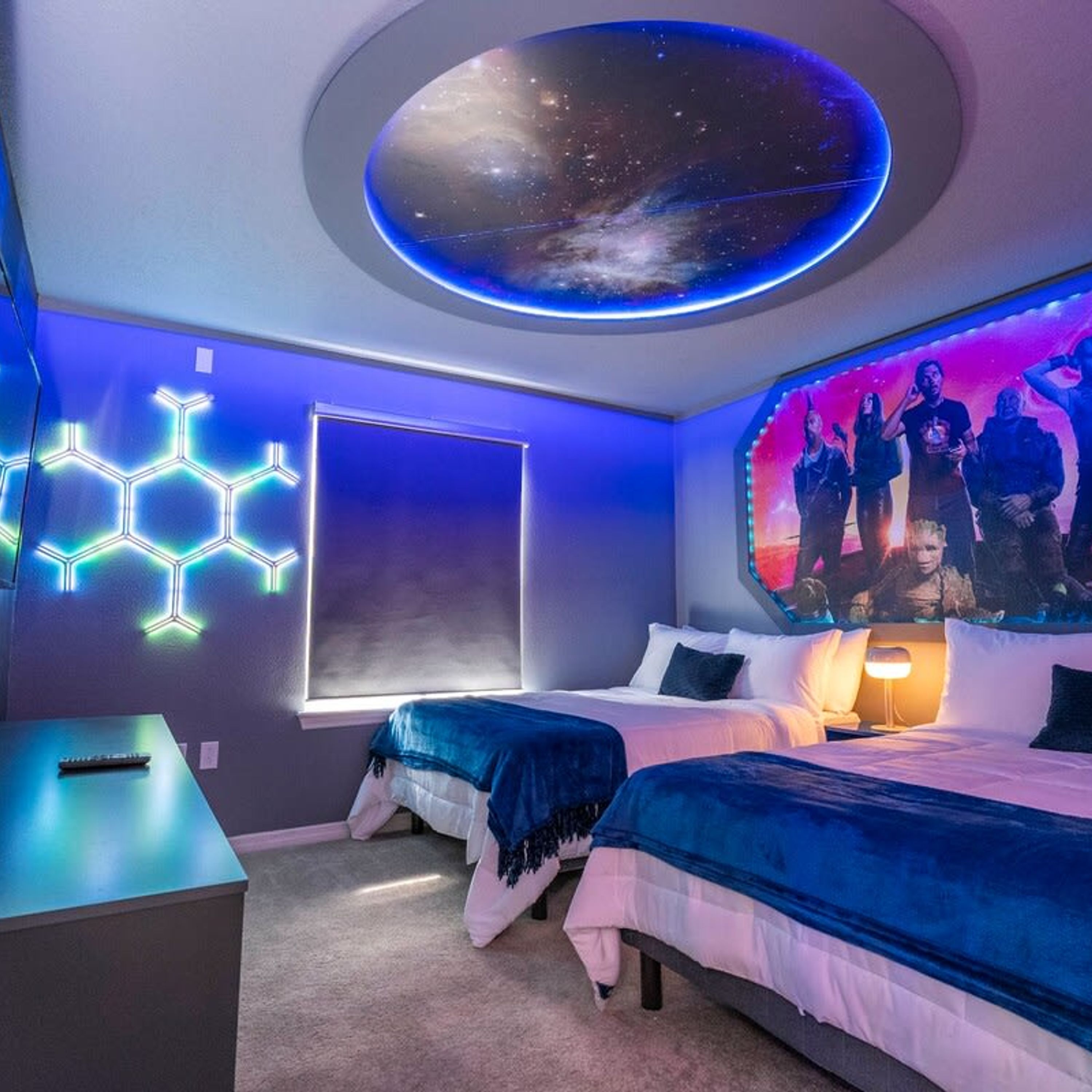 A bedroom with two beds, a desk, and a large window.