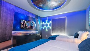 Ein modernes Schlafzimmer mit einem großen Bett, einer galaxie-dekorierten Decke, einem an der Wand montierten Fernseher und einer ungewöhnlichen, sechseckigen Leuchte.