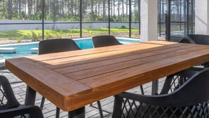 Eine Außenpatio mit Holztisch und -stühlen, einer Glasveranda und Blick auf Pool und Wald.