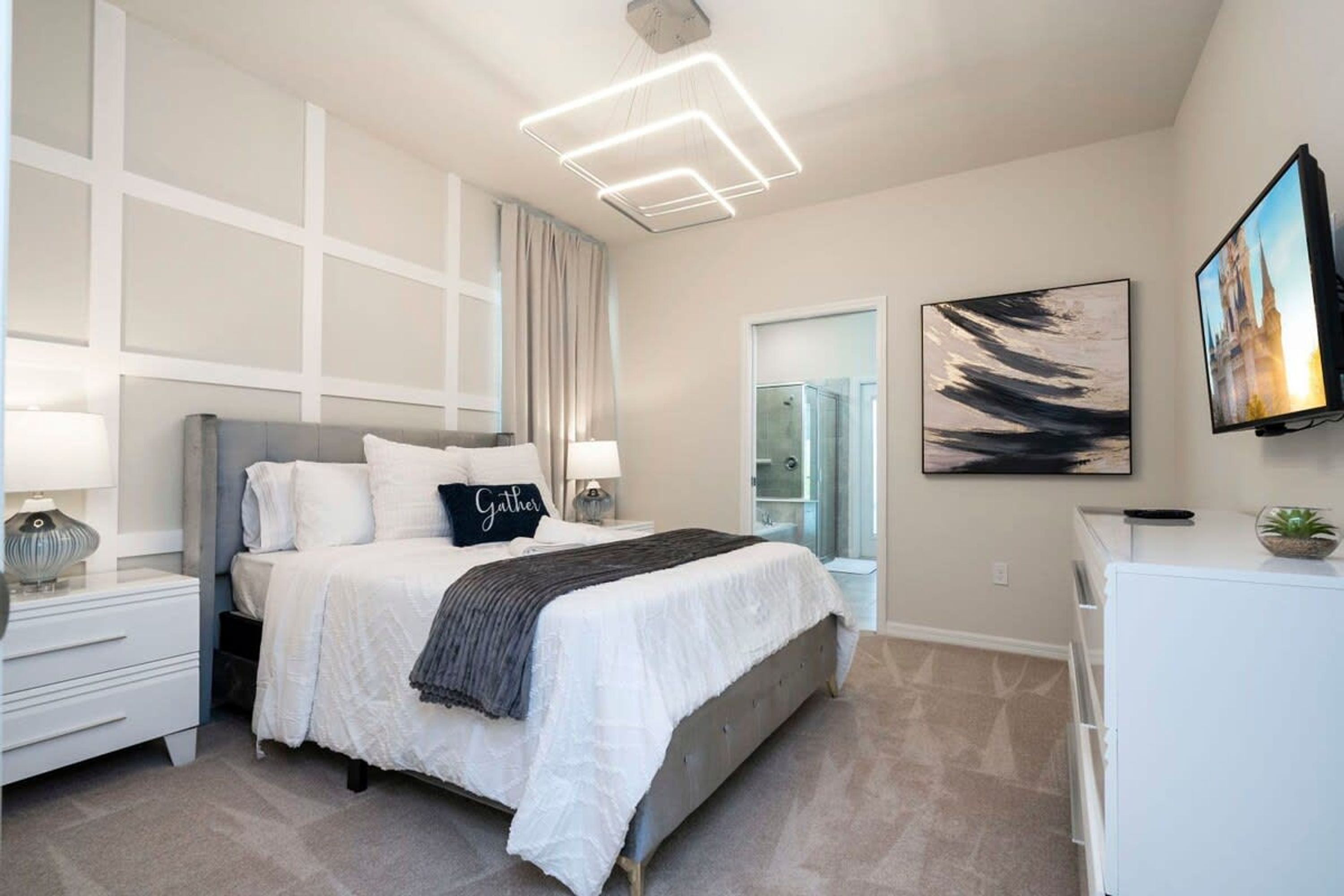 A modern bedroom with a bed, bedside tables, a TV, and artwork on the walls.