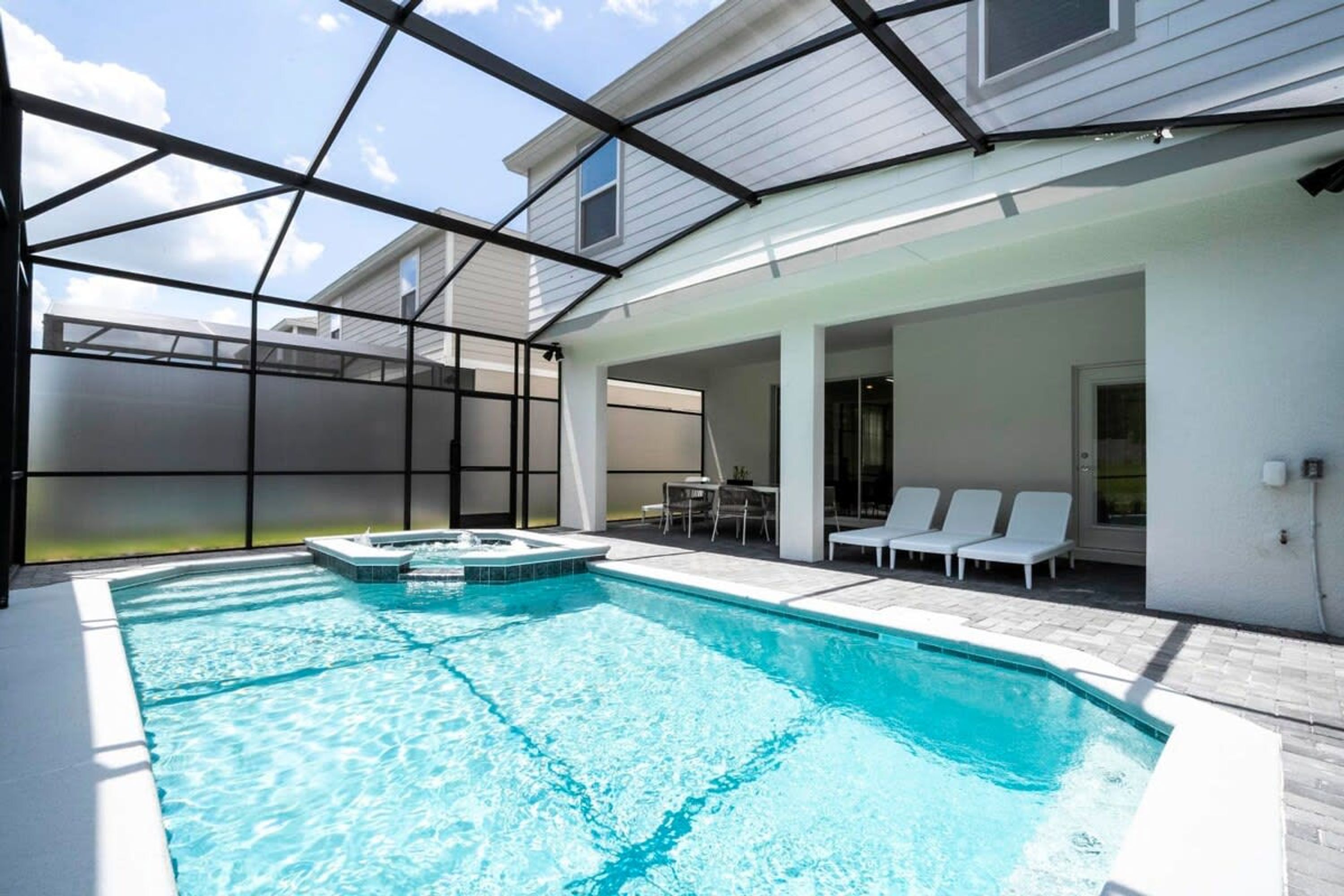 A swimming pool with a hot tub, surrounded by a covered patio area with lounge chairs and a table.