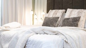 A bedroom with a large bed, white curtains, and a dark headboard.