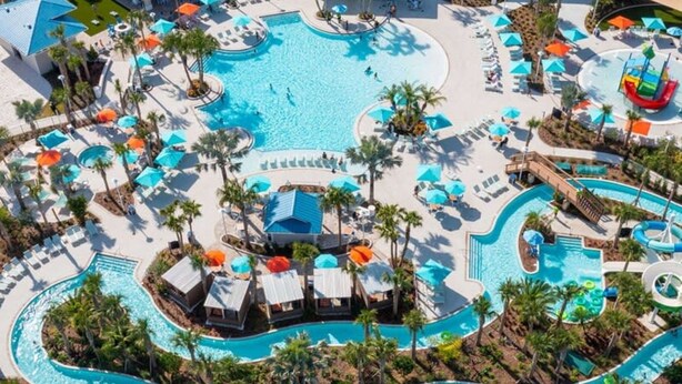 An aerial view of a resort with multiple swimming pools, sun loungers, and palm trees.