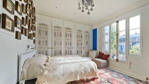 A bedroom with a large bed, a patterned rug, a wall of framed pictures, and a window with a view of buildings. - Stylish 5 Bed House in St John s Wood Maida Vale (London)