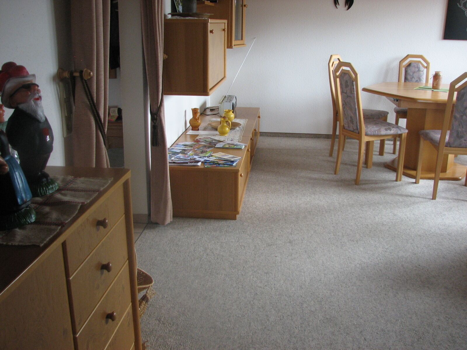 A room with a wooden table, chairs, a cabinet, and a small shelf with decorative items.