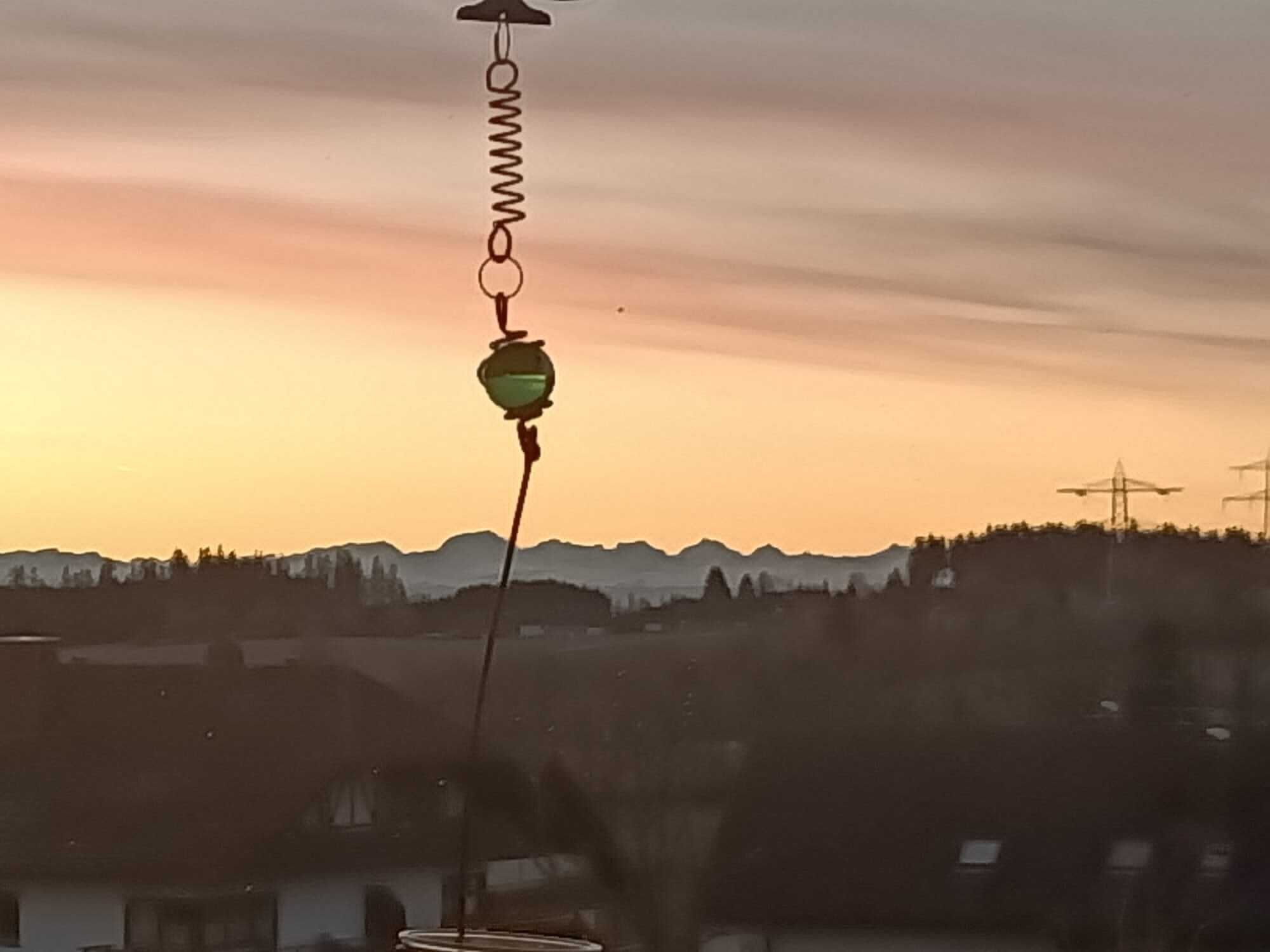 En vy över ett bergigt landskap i solnedgång, med ett hus som har ett synligt fönster och en hängande lampa.