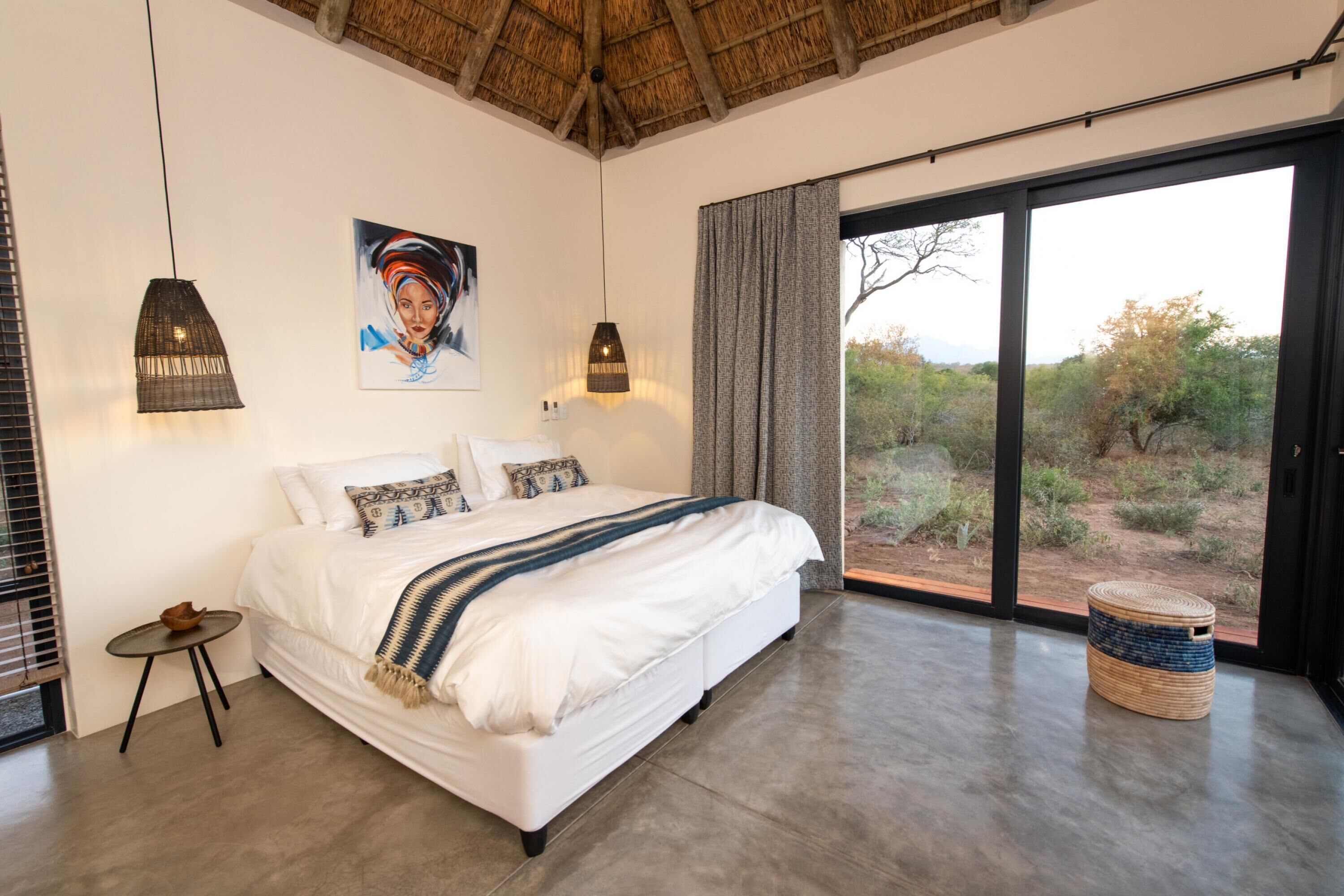 A bedroom with a large bed, a painting on the wall, and a view of the outdoors through a sliding door.