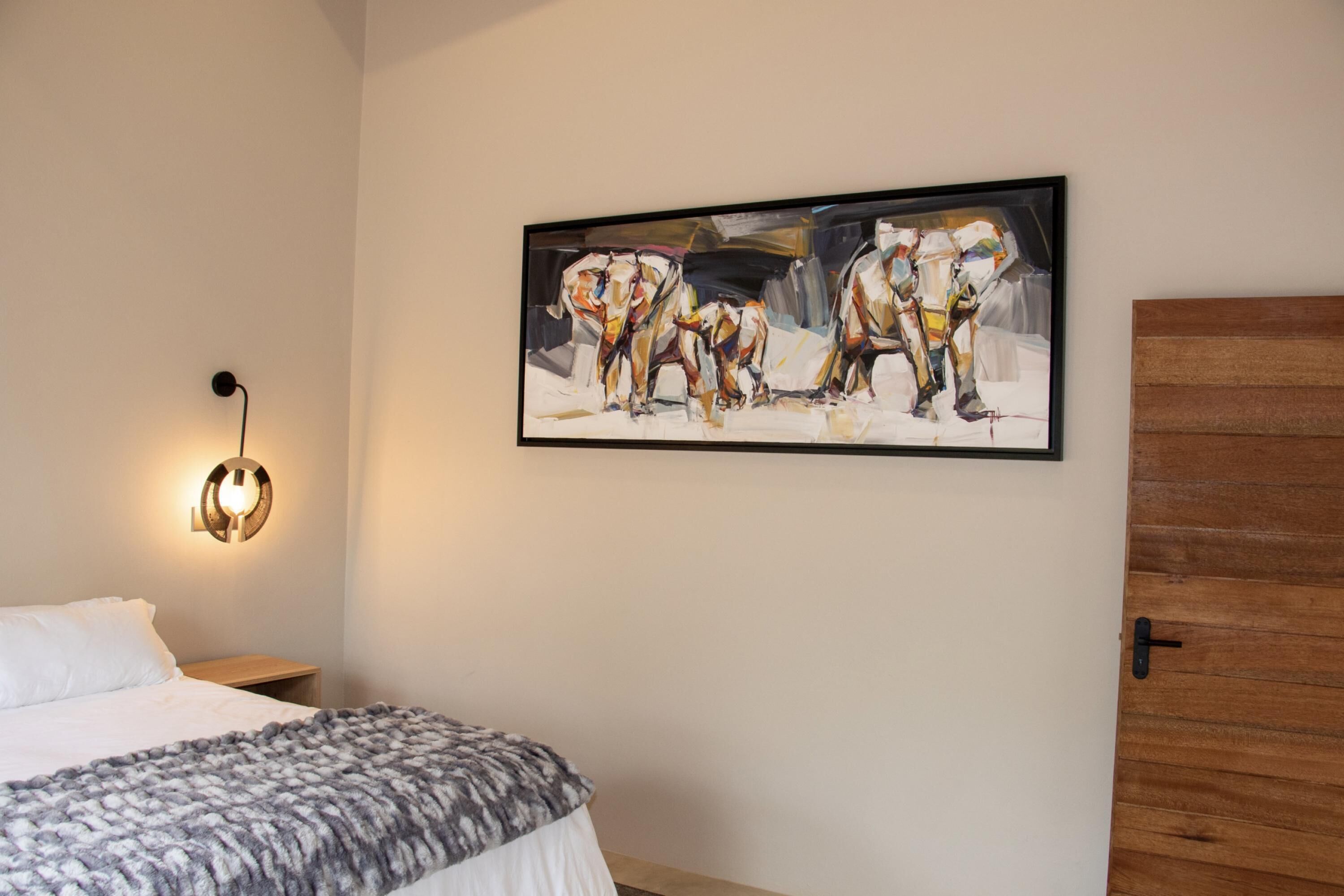 A bedroom with a bed, a wall-mounted painting, a nightstand, and a wooden door.
