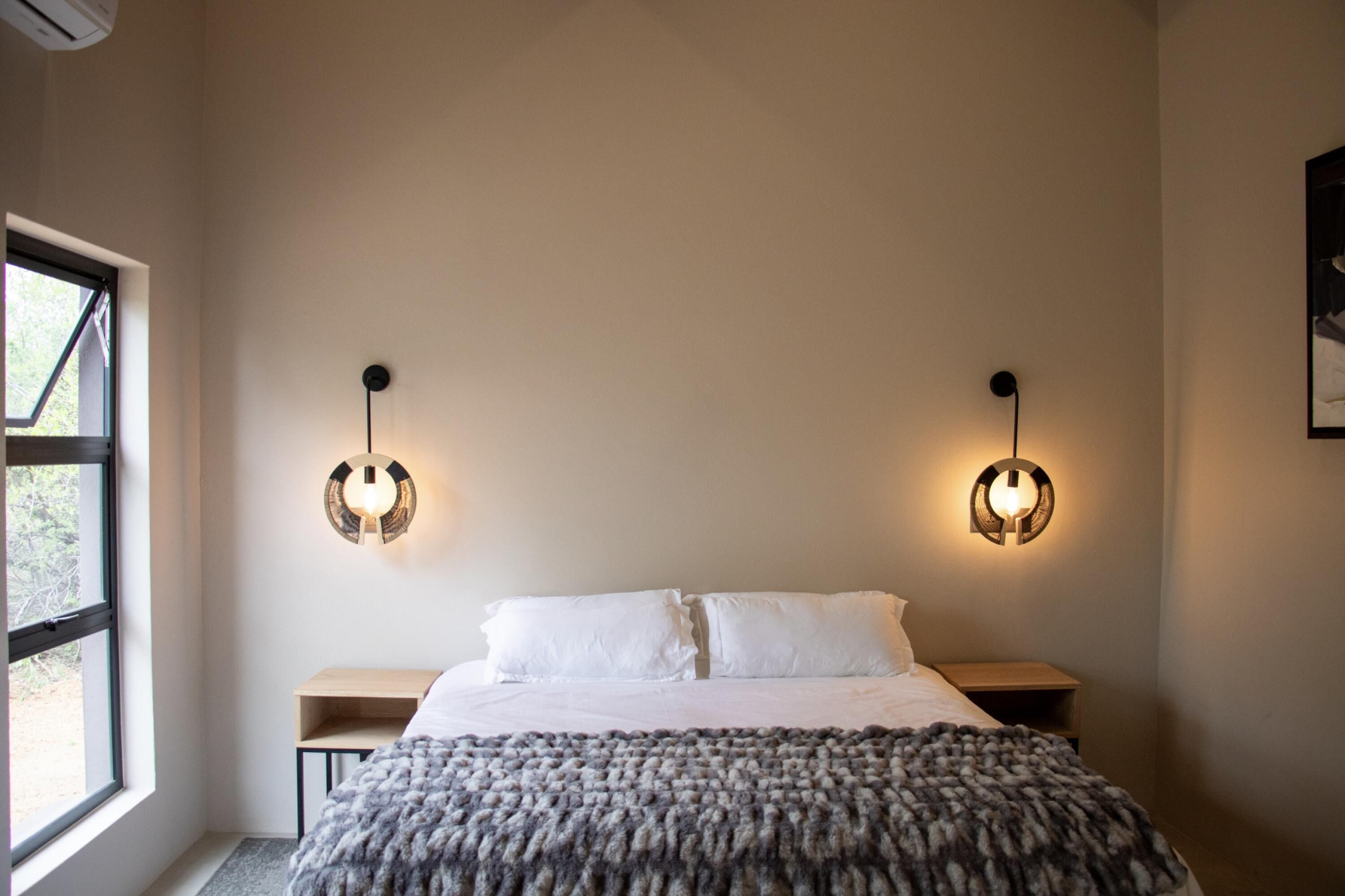 Une chambre à coucher comprenant un lit, deux tables de chevet, une fenêtre et des luminaires fixés au mur.