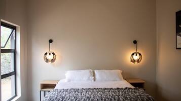 Une chambre à coucher comprenant un lit, deux tables de chevet, une fenêtre et des luminaires fixés au mur.