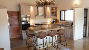 A modern kitchen with a central island, bar stools, and a large window providing natural light.