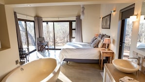A modern bedroom with a large bathtub, a double bed, and a bathroom with a large sink.