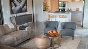 Un salon moderne avec un canapé, des fauteuils, une table basse et une cuisine en arrière-plan.