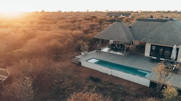 A modern house with a pool, outdoor seating, and a thatched roof.