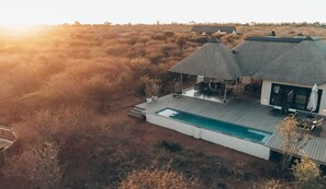 Ein modernes Haus mit Pool, Sitzgelegenheiten im Freien und einem Strohdach.