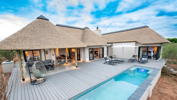 Une villa moderne dotée d’une piscine, d’un espace salon extérieur et d’un toit de chaume.