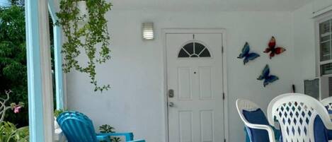 A covered porch with blue chairs and a white door.