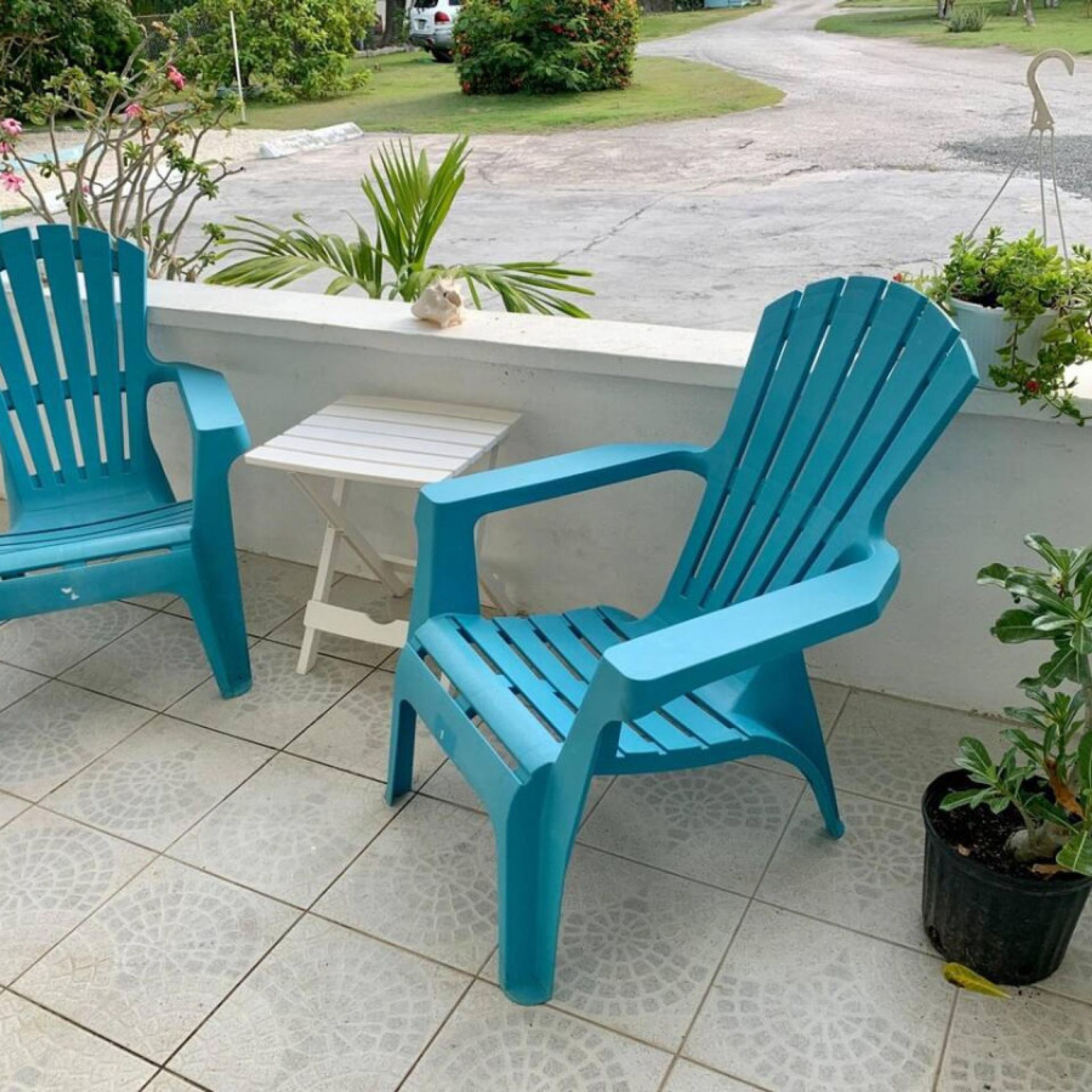Een balkon met twee turquoise stoelen en een witte tafeltje, omringd door planten en uitzicht op een straat.