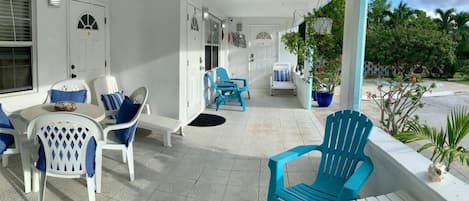 A covered outdoor seating area with white and blue chairs, a small table, and potted plants.