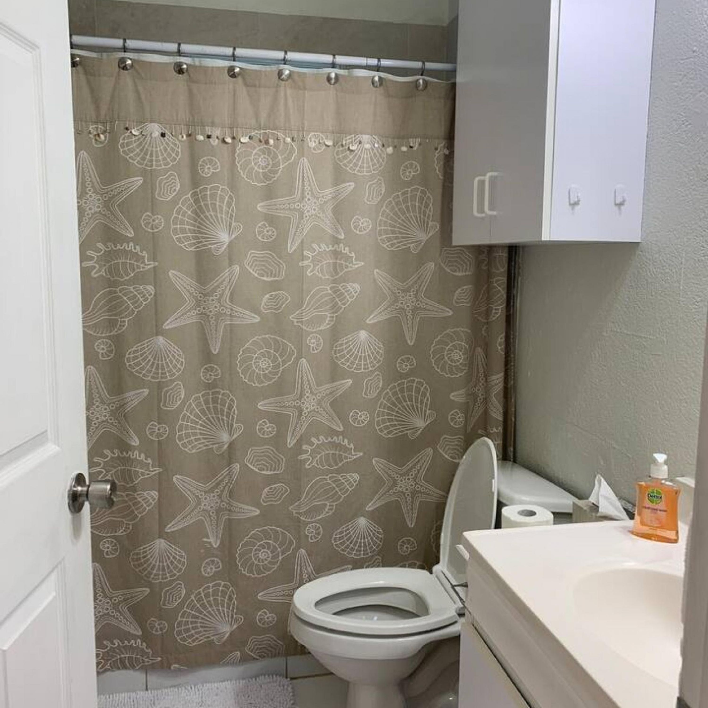 Un baño con cortina de ducha decorada con criaturas marinas, un inodoro, un lavabo y un dispensador de jabón.
