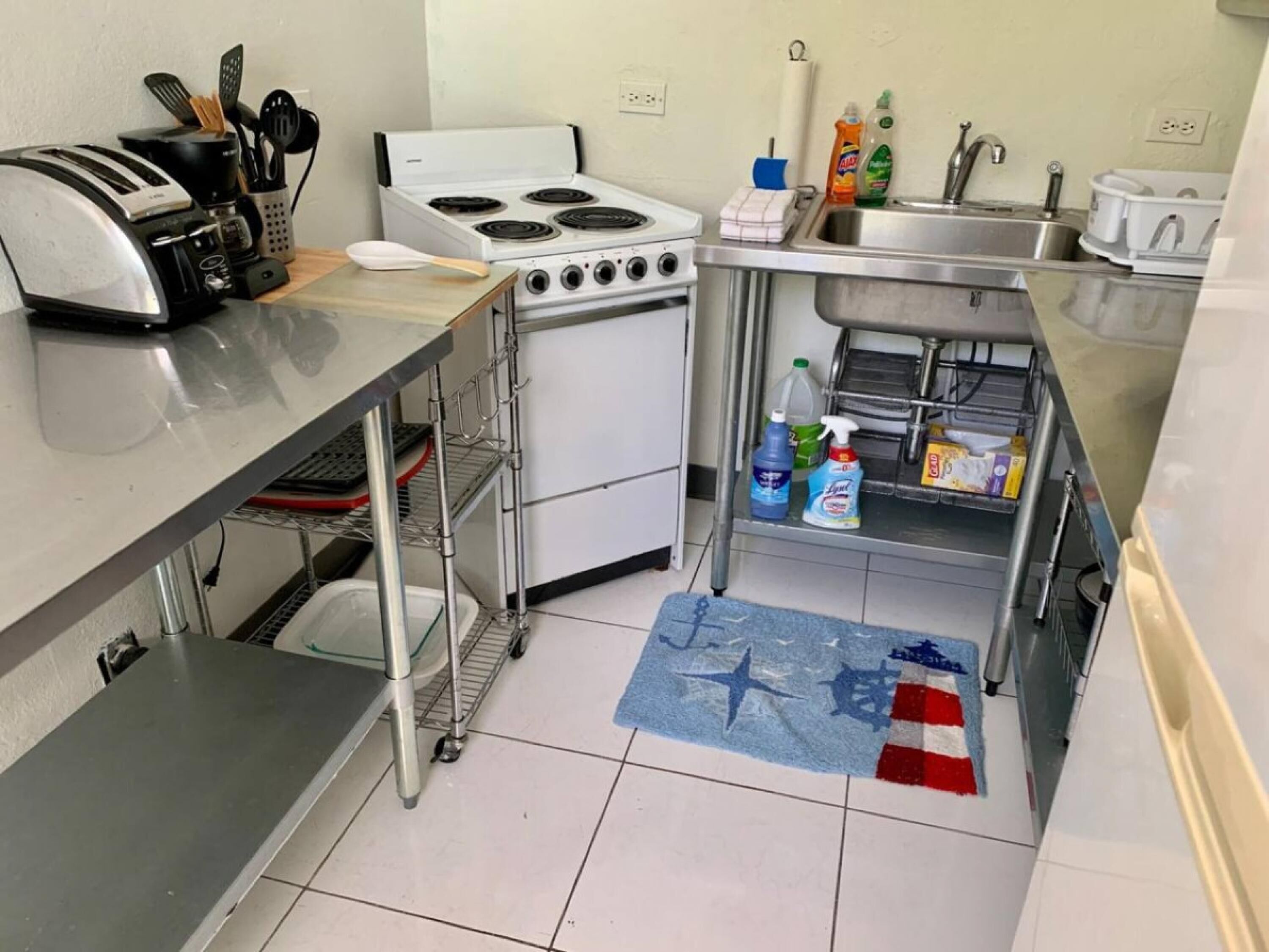 Una cocina compacta con tostadora, estufa, lavamanos y diversos productos de limpieza.