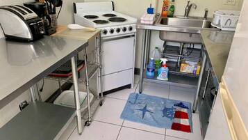 Una cocina compacta con tostadora, estufa, lavamanos y diversos productos de limpieza.