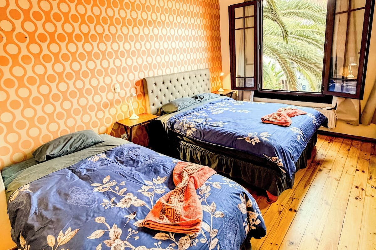 A room with two beds, a patterned wall, and a window with a view of palm trees.