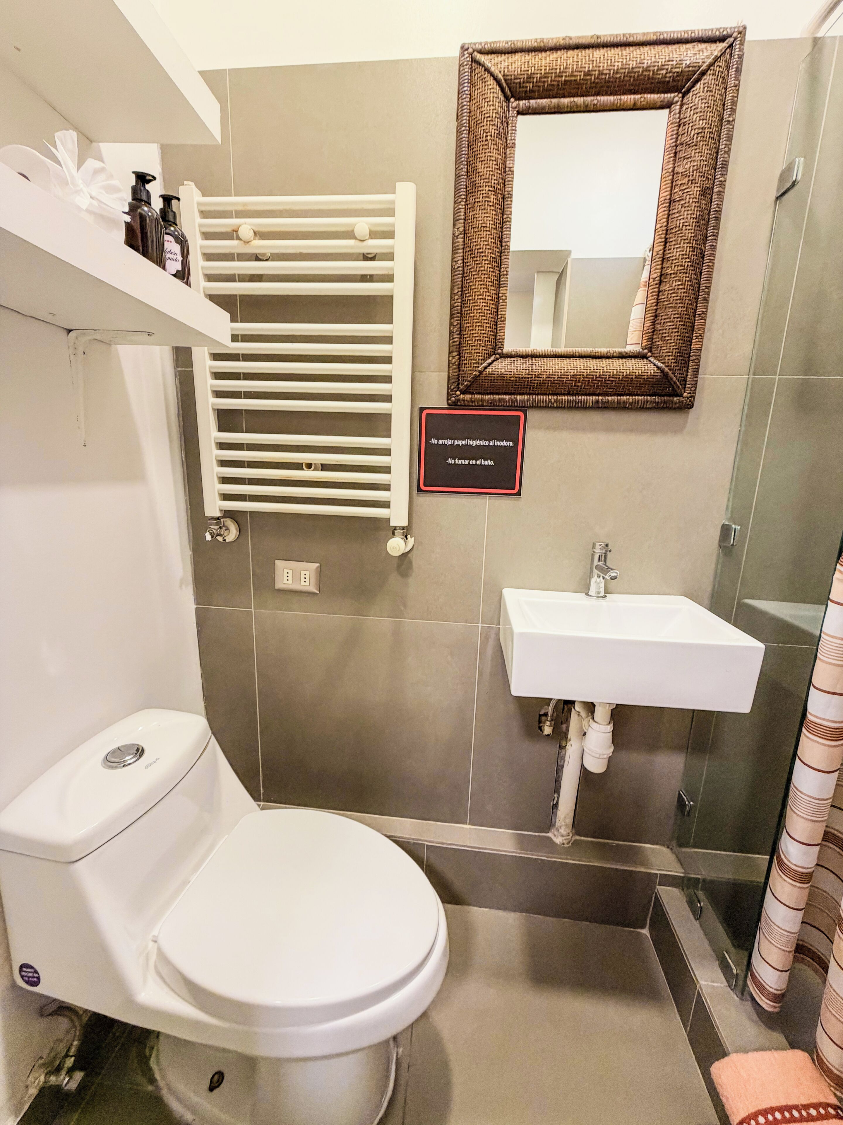 A bathroom with a toilet, a sink, a towel rack, a mirror, and a sign with hygiene instructions.