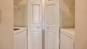 Uma lavanderia com duas portas brancas, uma máquina de lavar e uma secadora.
