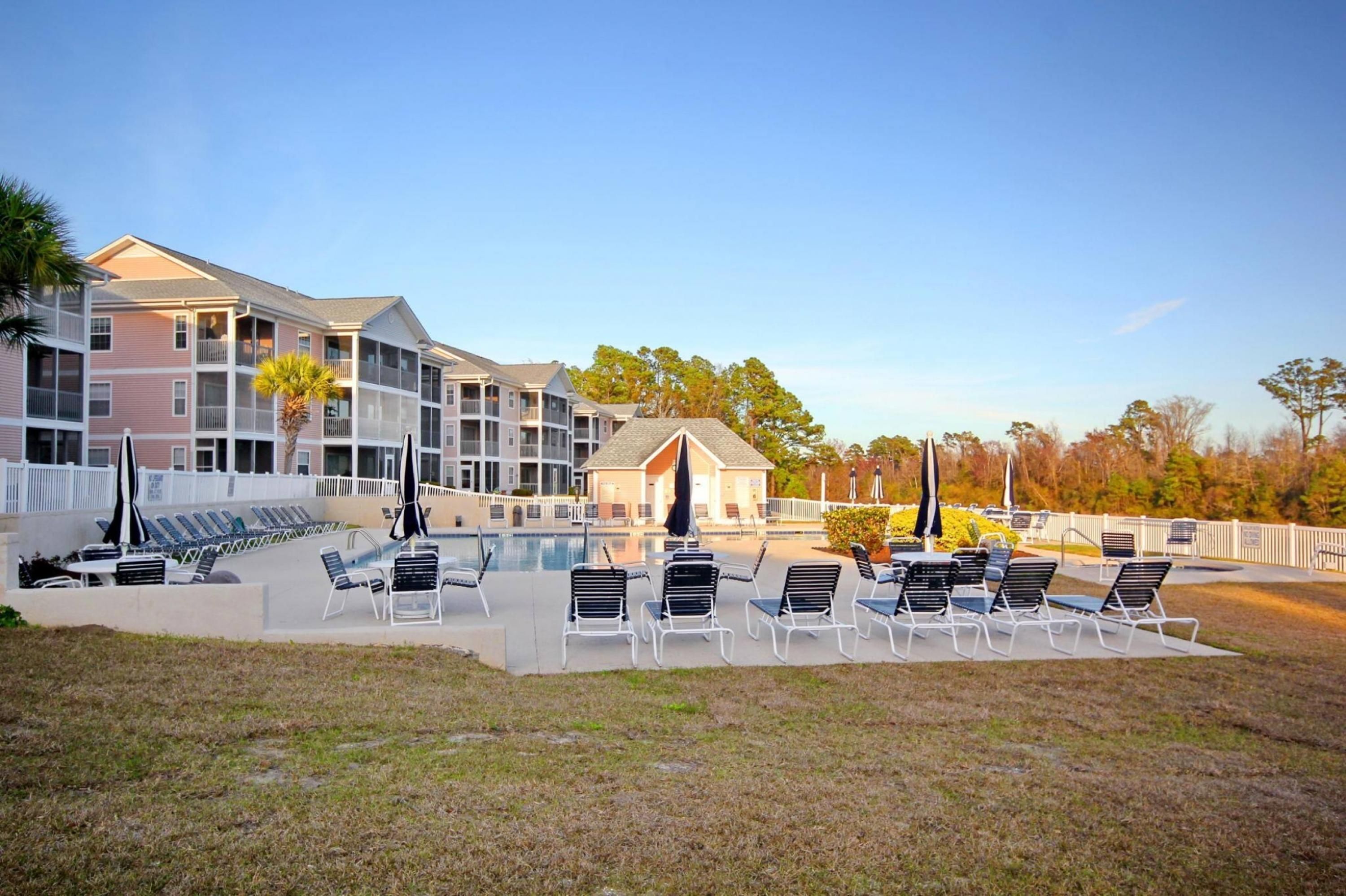 A hotel with a swimming pool, lounge chairs, and a covered area.