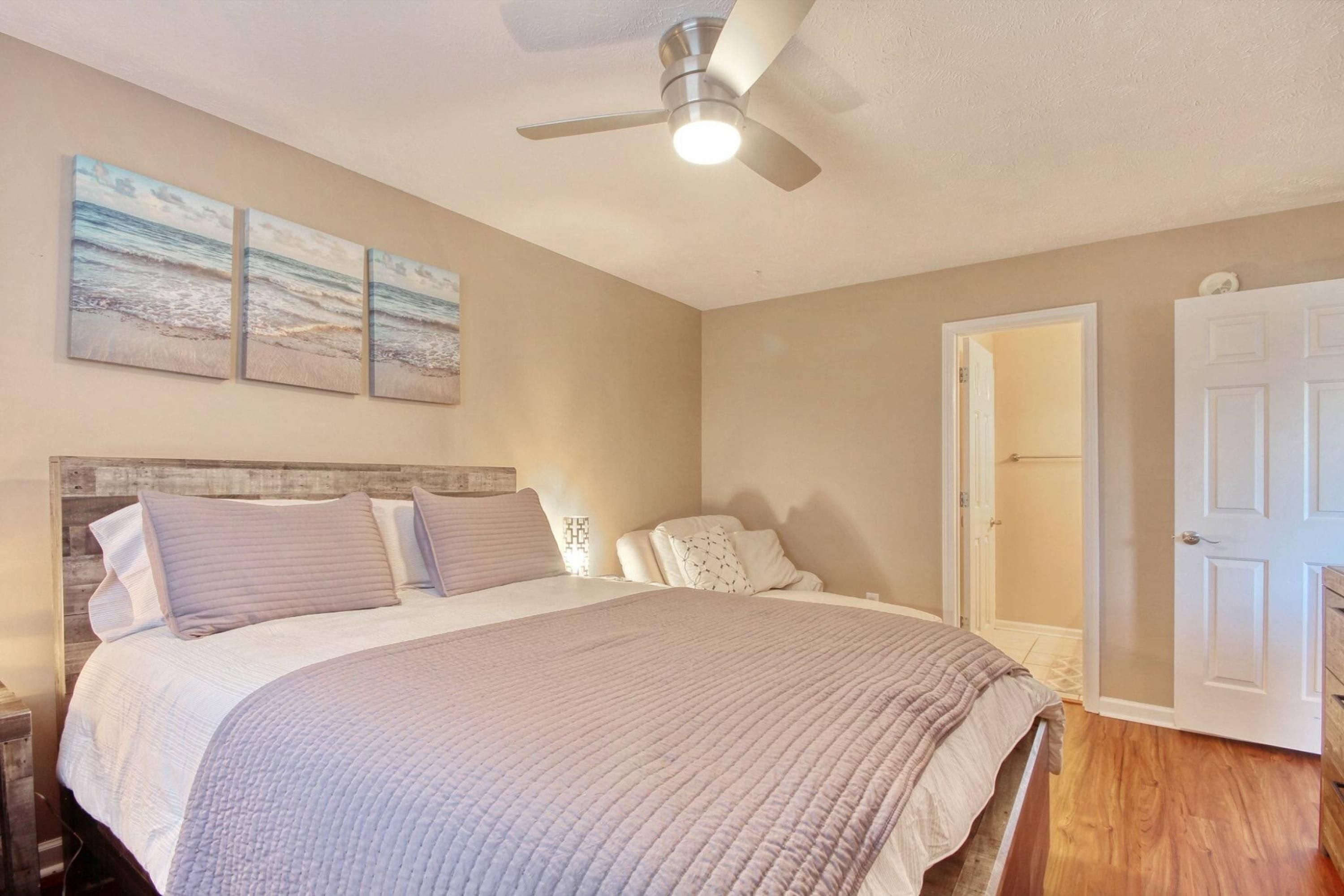 A bedroom with a bed, a ceiling fan, and three wall-mounted paintings.
